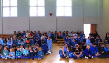 Dzieci siedzą po turecku na sali ubrane na niebiesko